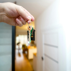 Hand holding house-shaped keychain inside new home.